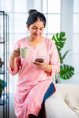 Téléchargez les photos : Indien jolie fille en utilisant smartphone pour faire du shopping, mesaging dans le salon - en image libre de droit
