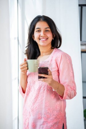 Photo for Indian pretty girl using smartphone for shopping, mesaging in living room - Royalty Free Image