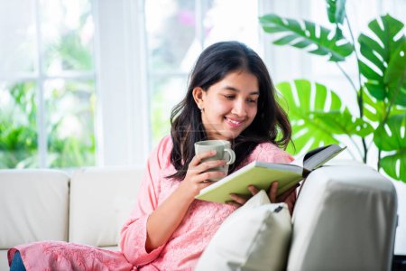 Foto de Chica joven bastante india leyendo libro o novela en casa - Imagen libre de derechos