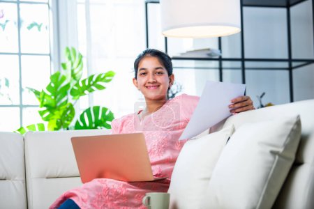 Indisches junges Mädchen arbeitet von zu Hause aus mit Laptop und Dokumenten
