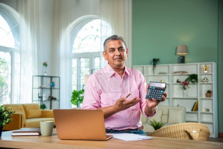Téléchargez les photos : Indien homme d'âge moyen travaillant sur ordinateur portable, smartphone avec des documents ayant café - en image libre de droit