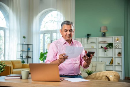Photo for Indian Mid age man working on laptop, smartphone with documents having coffee - Royalty Free Image