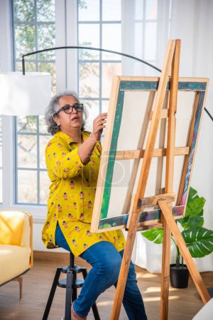 Téléchargez les photos : Indien Senior Artiste féminine travaillant sur la peinture en atelier sur chevalet - en image libre de droit