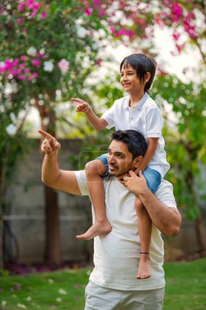 Foto de Vista lateral retrato de indio asiático padre llevar joven chico en espalda en el parque - Imagen libre de derechos