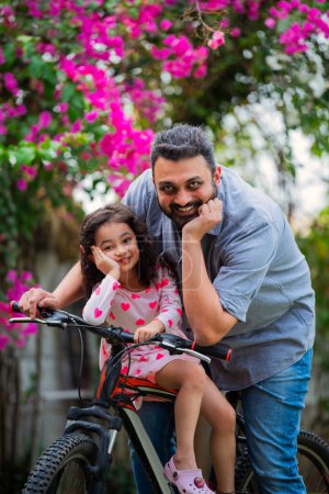 Photo for Portrait of Indian young girl and father riding on bicycle looking at camera - Royalty Free Image