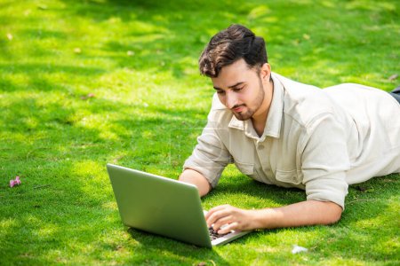 Photo for Young handsome Indian asian man using laptop in the park while lying on the grass - Royalty Free Image