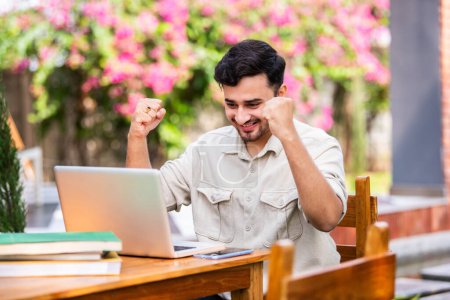 Téléchargez les photos : Asiatique indien mâle étudiant ou pigiste en utilisant ordinateur portable tout en étant assis sur la table à l'extérieur - en image libre de droit