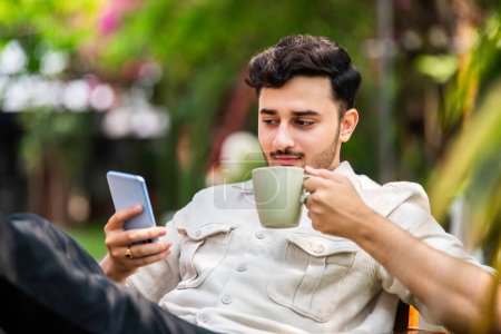 Foto de Hombre joven indio sentado y usando teléfono inteligente al aire libre - Imagen libre de derechos