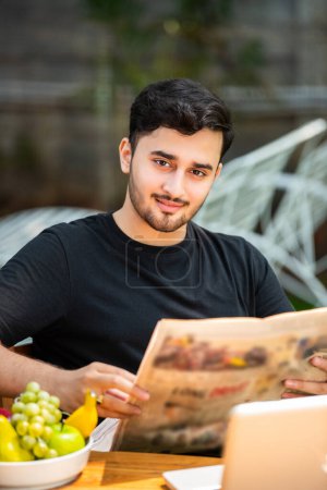 Photo for Indian young man reading news paper outdoors - Royalty Free Image