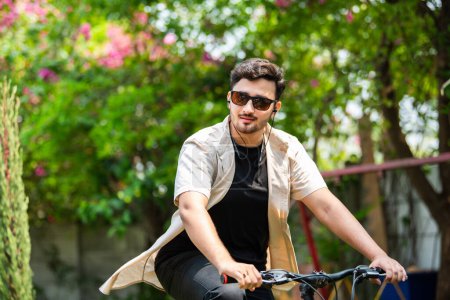 Téléchargez les photos : Asiatique indien jeune homme en utilisant smartphone tout en montant sur vélo - en image libre de droit