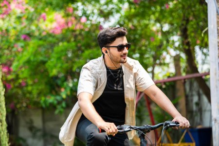 Téléchargez les photos : Asiatique indien jeune homme en utilisant smartphone tout en montant sur vélo - en image libre de droit