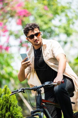 Photo for Asian indian young man using smartphone while riding on bicycle - Royalty Free Image