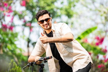 Foto de Asiático indio joven hombre usando smartphone mientras se monta en bicicleta - Imagen libre de derechos