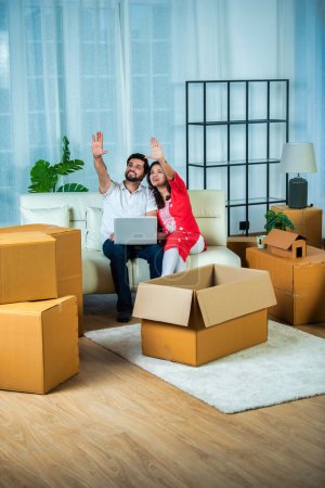 Photo for Indian young couple home moving or shifting concept, using laptop on sofa - Royalty Free Image
