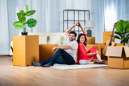 Foto de Concepto de movimiento de la casa, pareja joven india sentada en el piso de la sala de estar con cajas de cartón - Imagen libre de derechos