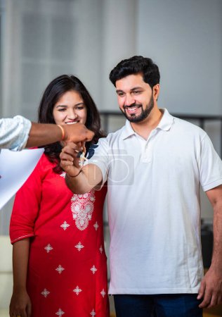 Happy Indian young couple taking keys of their new house from broker and smiling