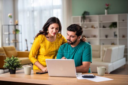 Foto de Feliz joven pareja casada india sentarse en la mesa calcular los gastos utilizar fácil servicio de banca en línea en casa - Imagen libre de derechos