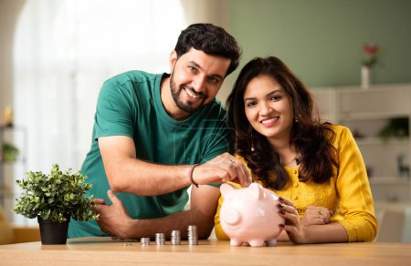 Indian asian young couple and saving concept using coins and piggy bank at home