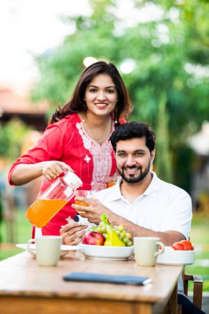 Téléchargez les photos : Indien mari et femme avoir jus de fruits frais dans le petit déjeuner tandis que assis à la table à l'extérieur - en image libre de droit