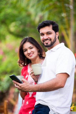 Téléchargez les photos : Jeune couple indien utilisant téléphone intelligent et tablette PC dans le café extérieur - en image libre de droit