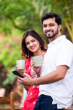 Photo for Young Indian couple using smart phone and tablet pc in the outdoor cafe - Royalty Free Image