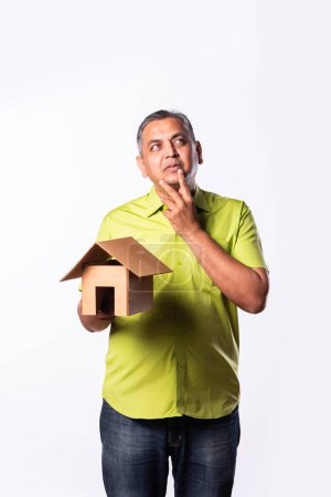Photo for Indian asian mid age man pointing, thinking while holding house made of cardboard - Royalty Free Image