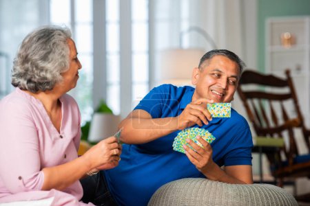 Photo for Mid age Indian asian couple enjoying playing cards together at home - Royalty Free Image