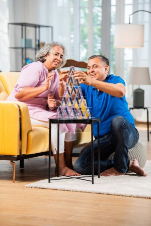 Téléchargez les photos : Couple indien d'âge moyen construire une maison en utilisant des cartes à jouer et avoir du plaisir - en image libre de droit