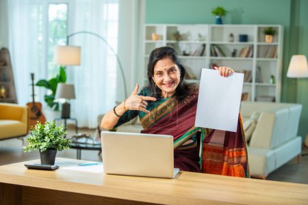Téléchargez les photos : Senior Indien asiatique femme à l'aide d'ordinateur portable et de papiers pour la comptabilité à la maison - en image libre de droit