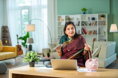 Téléchargez les photos : Indien asiatique vieille dame avec tirelire, ordinateur portable, argent et modèle de maison 3D à la maison - en image libre de droit