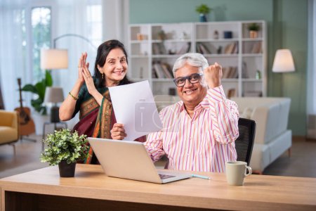 Photo for Retired Indian asian couple do paperwork at home with laptop, piggy bank, currency notes, documents - Royalty Free Image