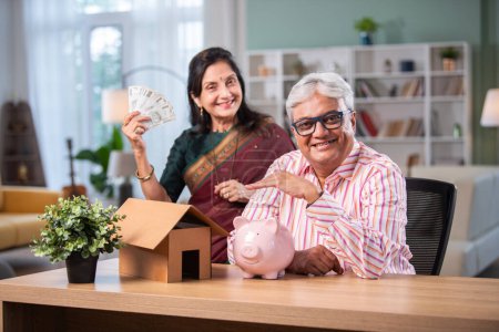 Rentner indisches asiatisches Paar erledigt Papierkram zu Hause mit Laptop, Sparschwein, Geldscheinen, Dokumenten