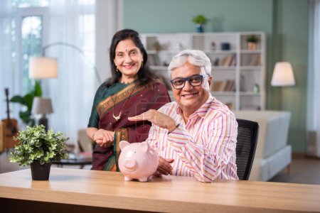 Téléchargez les photos : Retraité indien asiatique couple faire de la paperasse à la maison avec ordinateur portable, tirelire, billets de devises, documents - en image libre de droit