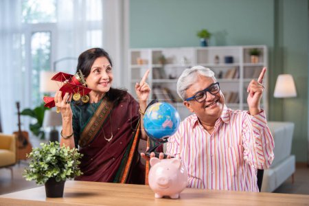 Photo for Indian senior retired couple planning Vacation with laptop, toy plane, globe model - Royalty Free Image