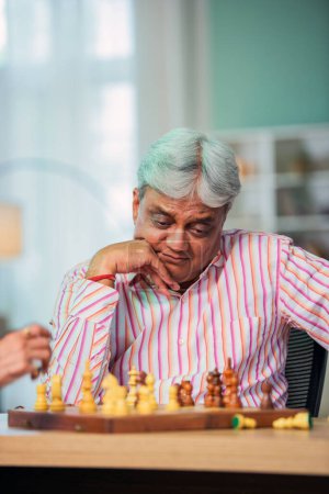 Téléchargez les photos : Senior indien asiatique couple jouer aux échecs ensemble à la maison sur la table - en image libre de droit