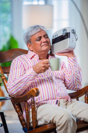Foto de Jubilado asiático indio hombre escuchar viejo canciones en vintage radio en casa - Imagen libre de derechos