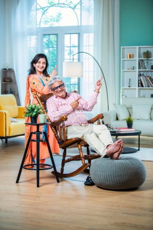 Téléchargez les photos : Couple indien mûr pointant quelque chose tout en étant assis à l'intérieur - en image libre de droit
