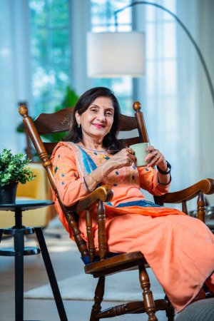 Téléchargez les photos : Indien asiatique senior femme boissons café, thé ou jus de fruits frais - en image libre de droit