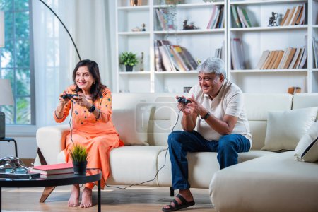 Foto de India Senior pareja divirtiéndose jugando videojuegos mientras se sienta en el sofá en casa - Imagen libre de derechos