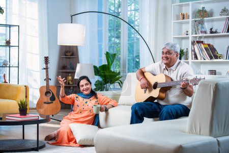 Photo for Elderly Indian asian couple singing a song together while playing guitar at home while enjoying leisure time - Royalty Free Image
