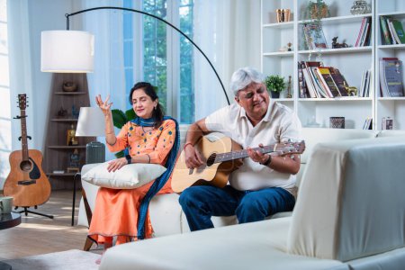 Photo for Elderly Indian asian couple singing a song together while playing guitar at home while enjoying leisure time - Royalty Free Image
