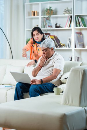 Indisches Paar im Ruhestand erledigt Papierkram zu Hause mit Laptop, Dokumente zu Hause auf dem Sofa
