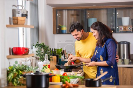 Photo for Happy loving Indian asian young couple cooking food in kitchen together, hugging, standing at table - Royalty Free Image