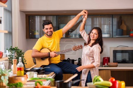 Téléchargez les photos : Indien jeune couple cuisine nourriture dans la cuisine, mari joue de la guitare et femme chante - en image libre de droit