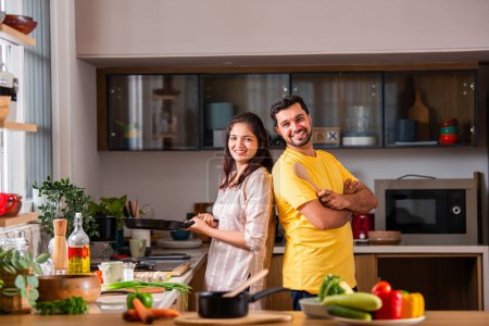 Téléchargez les photos : Heureux amour indien asiatique jeune couple cuisine nourriture dans cuisine ensemble, câlins, debout à table - en image libre de droit