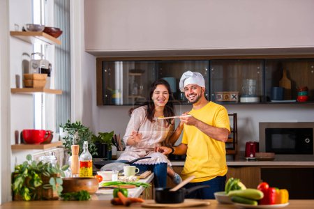 Photo for Happy loving Indian asian young couple cooking food in kitchen together, hugging, standing at table - Royalty Free Image