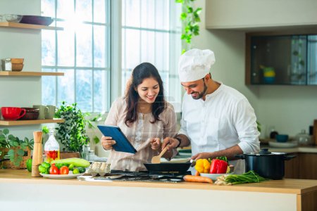Photo for Cheerful Indian Couple Using Digital Tablet While Cooking Healthy Lunch In Kitchen, Searching Recipe Online - Royalty Free Image