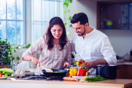 Téléchargez les photos : Heureux amour indien asiatique jeune couple cuisine nourriture dans cuisine ensemble, câlins, debout à table - en image libre de droit