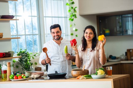 Foto de India asiático joven pareja holding fresco vegetal en cocina mientras cocinar alimentos - Imagen libre de derechos