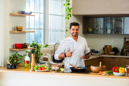 Foto de India guapo comida de cocina masculina en la cocina y el uso de la tableta PC - Imagen libre de derechos